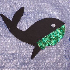 Image of whale created with foam sheet for body, googly eye, sequins for belly, and bubble wrap for background