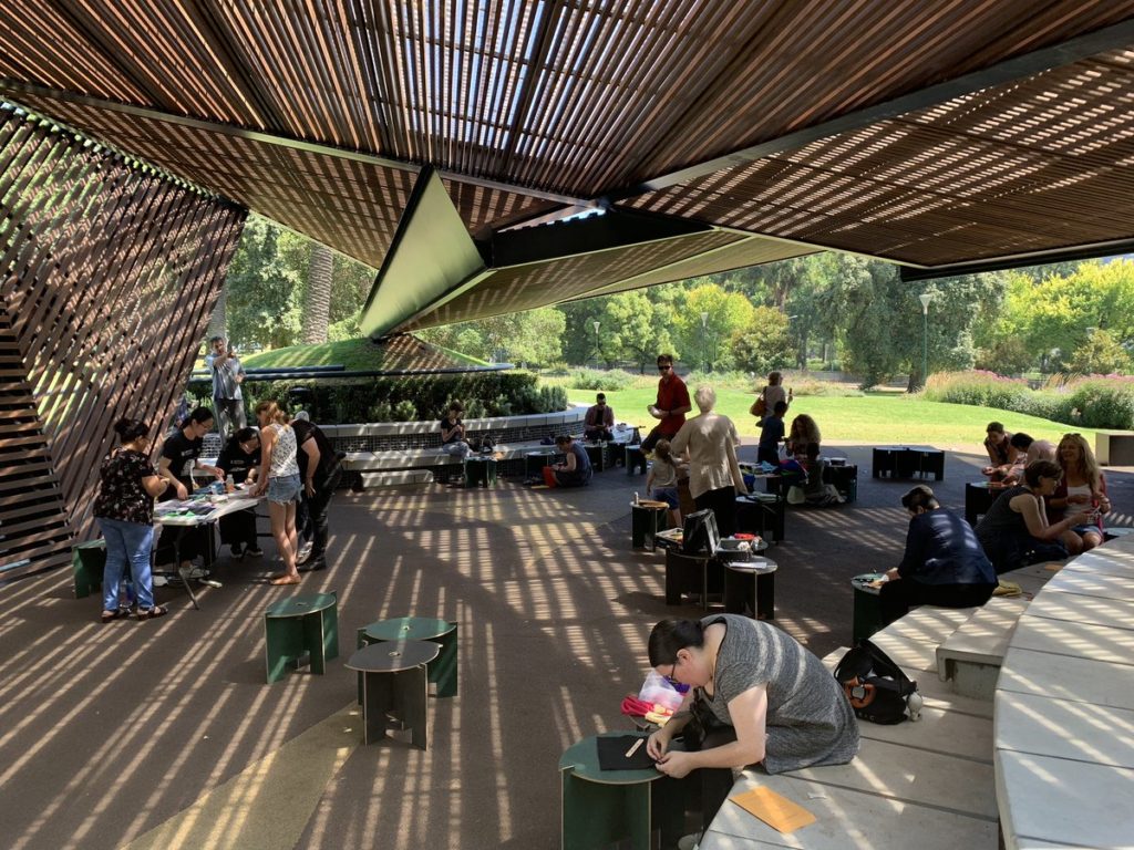 People sewing in MPavilion 2018, an open-air wooden architectural space. 