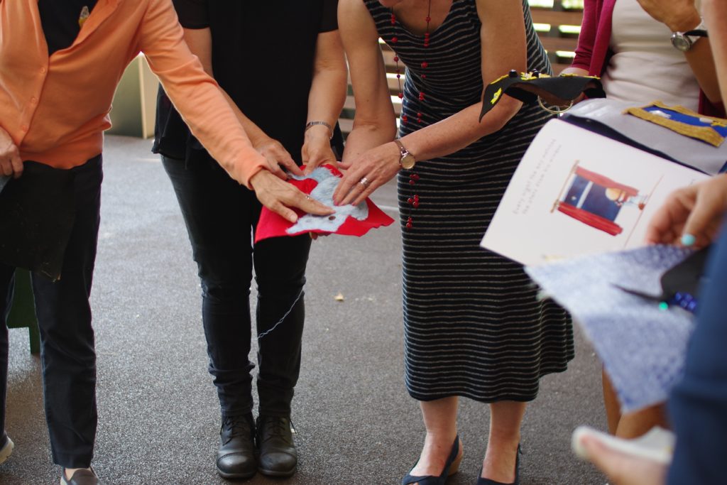 Workshop participants touching a page depicting a furry blue cat with googly eyes. 