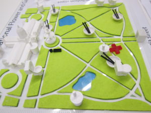 Map of Carlton Gardens with felt grass, a 3D printed building and fountain, and 3D printed icons for food, drinks, etc. 