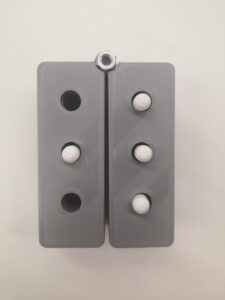 two rectangular prisms with 3 holes each, joined with a screw. They can sit together as a braille cell or swing out into a line. 