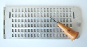 Metallic braille slate with stylus.