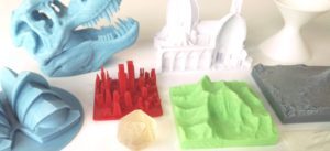 A selection of 3D printed plastic models, such as a braille dice, the Sydney Opera House, New York streetscape, Mount Everest, Mount Fuji, T-Rex skull, a cathedral and a mathematical shape. 